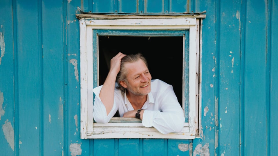 Foto vom Event mit Christian Maier: Schokoladenseit’n, mit dem Künstler am Fenster und einer blauen Wand.