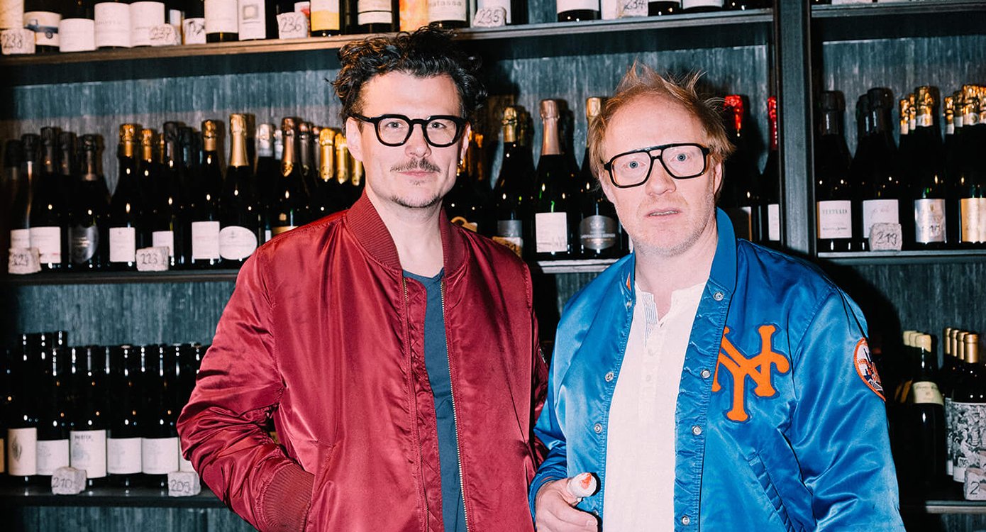 zwei Männer mit Brillen, der eine trägt eine rote, der andere eine blaue Jacke