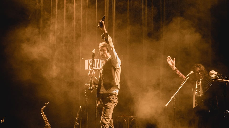 Szenenfoto von Gankino Circus bei einer Bühnenaufführung mit Musikern im Scheinwerferlicht.