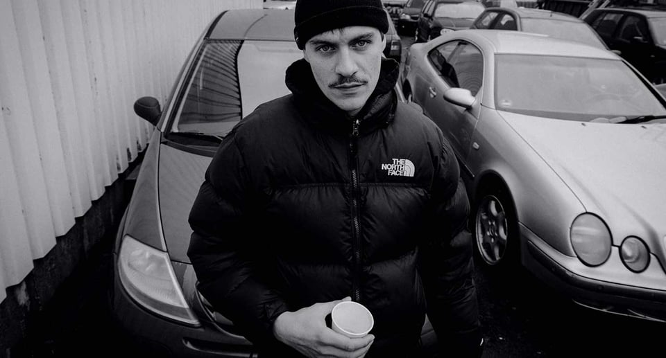 Ein Schwarzweißfoto des Künstlers mit ein paar Autos im Hintergrund