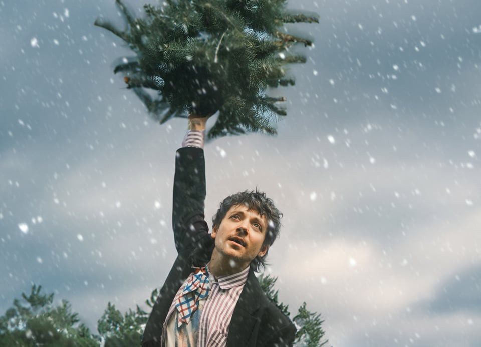 Foto eines Mannes mit einem Weihnachtsbaum in der Hand und im Hintergrund ein schneebedeckter Himmel