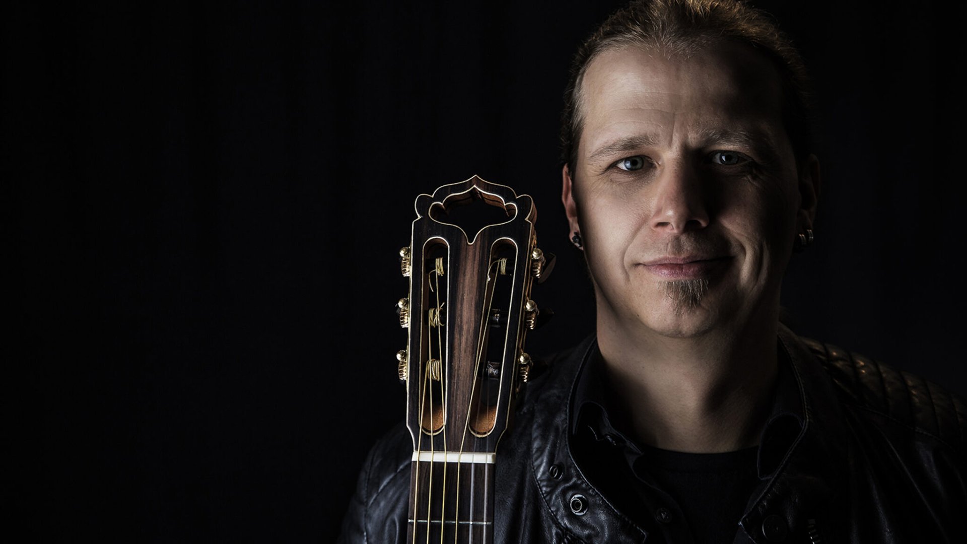 Stefan Eichner mit Gitarre vor schwarzem Hintergrund, Nahaufnahme, Pressebild für sein Reinhard-Mey-Tribute-Konzert.