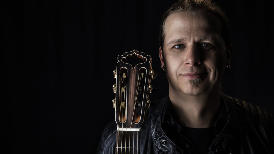 Stefan Eichner mit Gitarre vor schwarzem Hintergrund, Nahaufnahme, Pressebild für sein Reinhard-Mey-Tribute-Konzert.