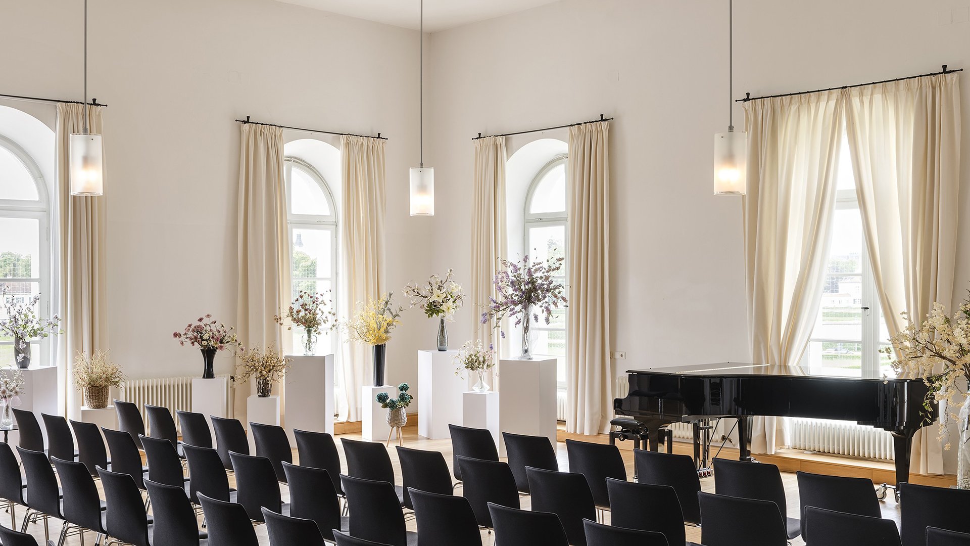 Der Konzertsaal mit Flügel und Stühlen sowie mehreren japanische Blumenkunst-Gestecken
