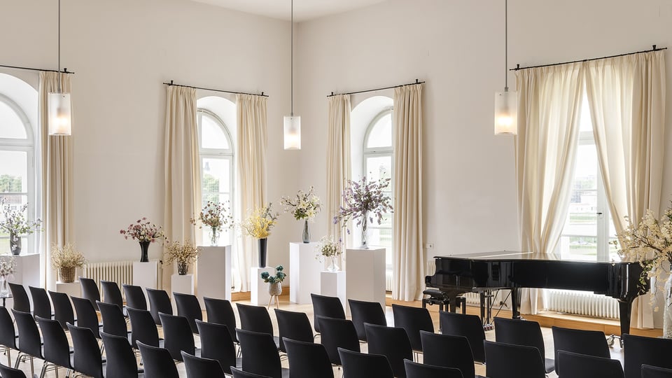 Der Konzertsaal mit Flügel und Stühlen sowie mehreren japanische Blumenkunst-Gestecken