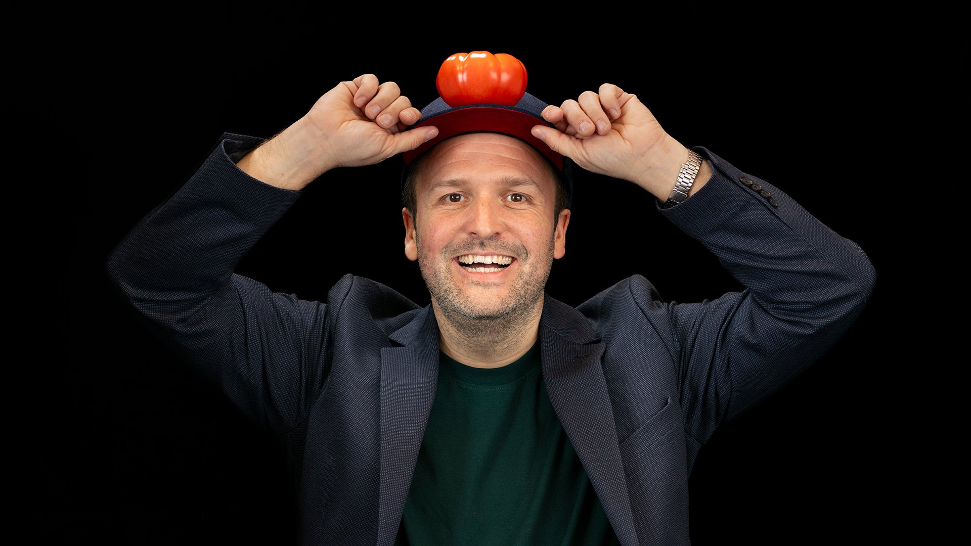 Foto von der Veranstaltung Christian Bumeder alias BUMILLO - Meister Bumeder mit dem Künstler mit einer Tomate auf dem Kopf vor schwarzem Hintergrund