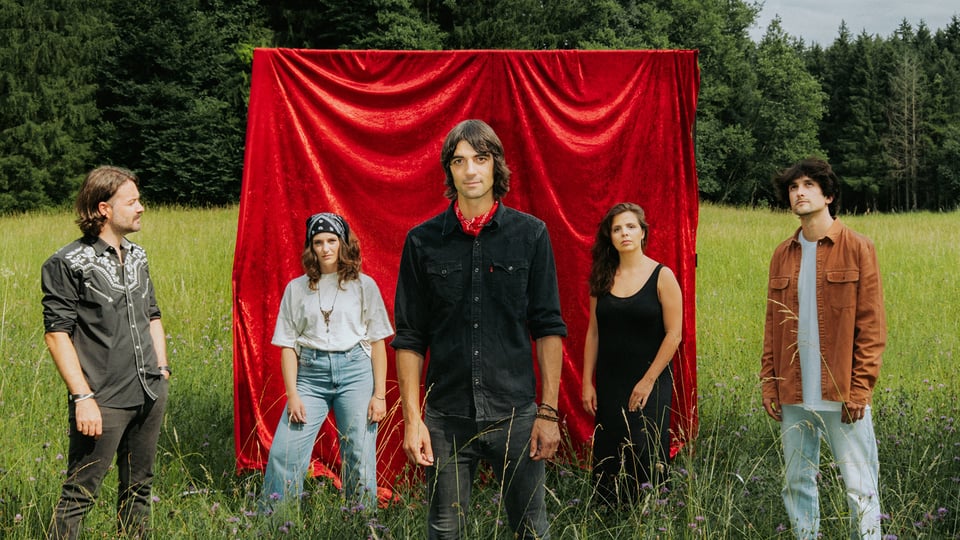 Foto für die Veranstaltung Max von Milland & Die Brennenden Herzen, mit der Band in der Natur und hinter ihnen einem roten Vorhang.