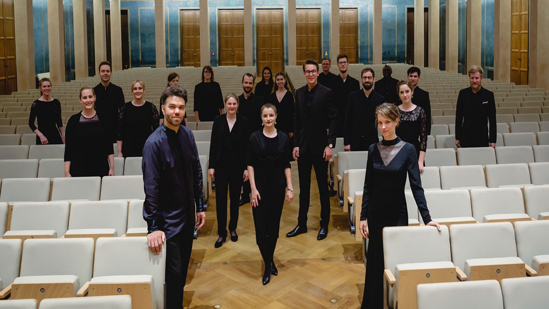Foto für das Event der Camerata Vocale München mit der Gruppe in schwarzer Kleidung zwischen weißen Sitzreihen.