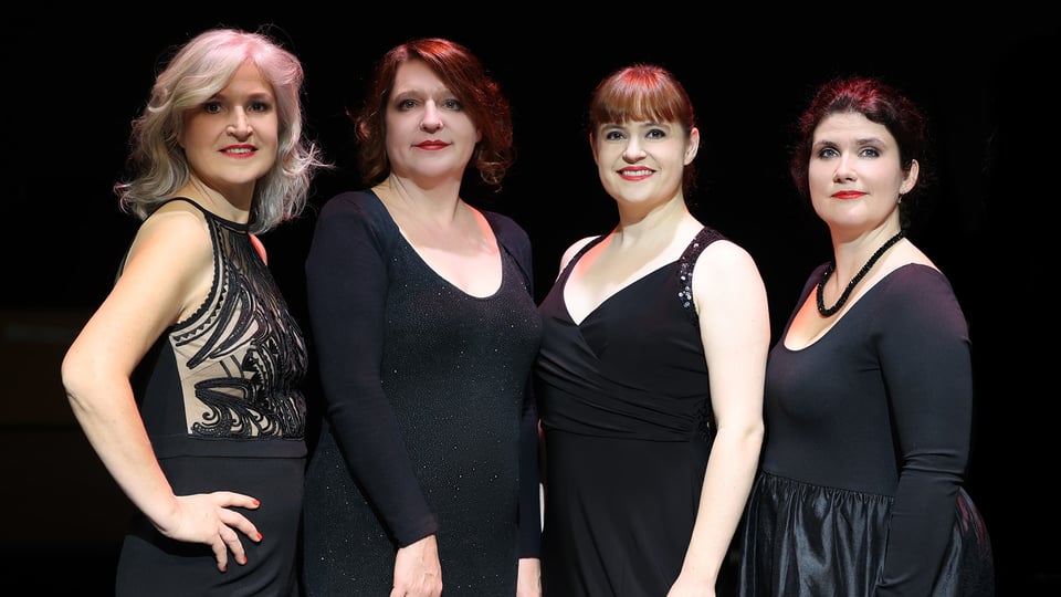 Foto für die Veranstaltung von Vokal Total – Aquabella, mit vier Frauen in Schwarz gekleidet vor schwarzem Hintergrund