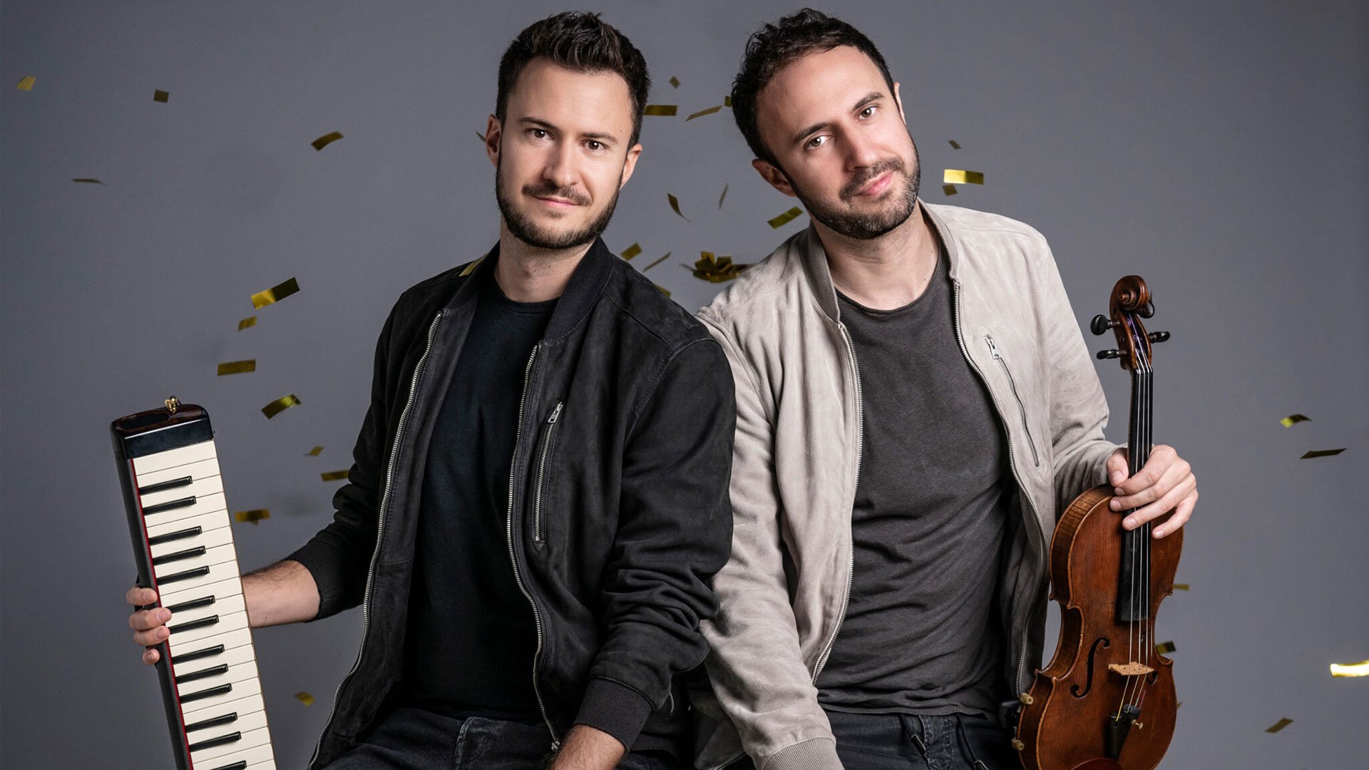 Foto für die Veranstaltung von Ass‑Dur mit den beiden Künstlern, die Instrumente in den Händen halten, vor einem grauen Hintergrund
