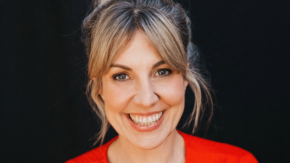 Portrait von Nora Boeckler in einem knallig rotem Oberteil, wie sie gerade in die Kamera blickt vor einem schwarzem Hintergrund