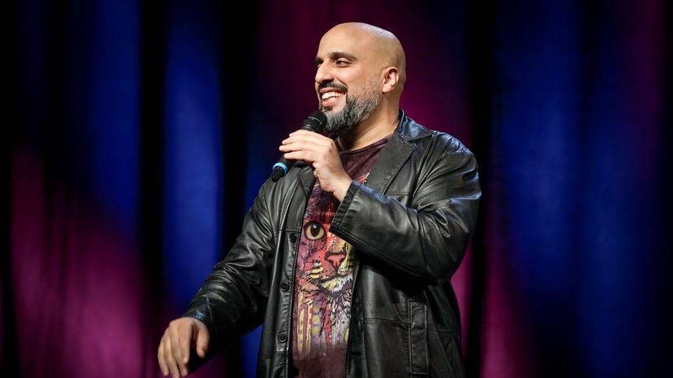 Foto für das Event Abdelkarim – Plan Z – jetzt will er’s wissen! mit dem Künstler, der ein Mikrofon in der Hand hält und vor einem Vorhang steht