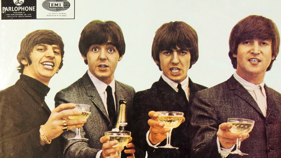 Ein Foto der Beatles in dunklen Anzügen mit Gläsern in den Händen 