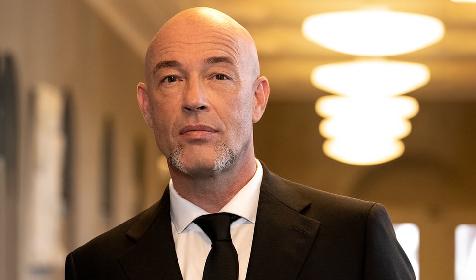 Ein Portrait des Künstlers in eine schwarzen Anzug in einem Flur mit Deckenbeleuchtung