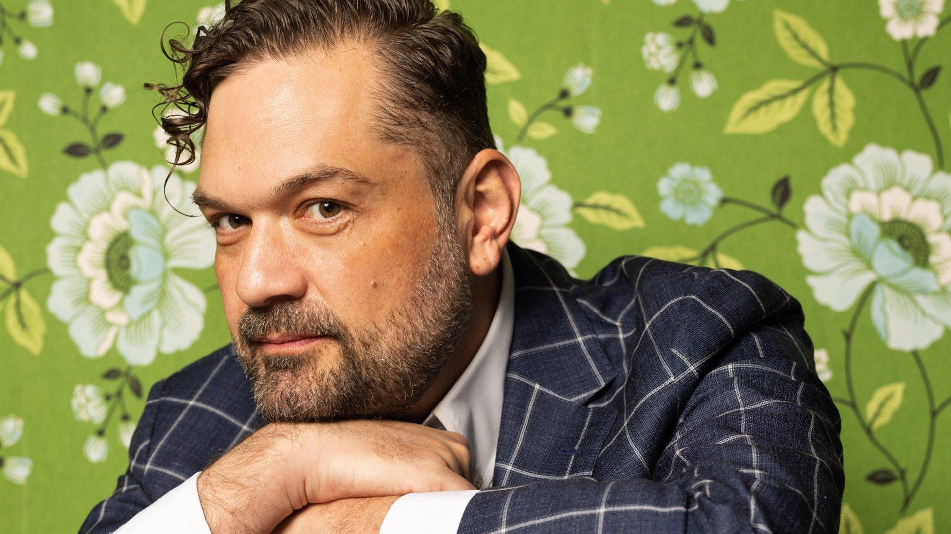 Foto für die Veranstaltung ‚Lesung mit Anton Leiss-Huber‘ – der Künstler vor einer grünen Wand mit gemalten Blumen