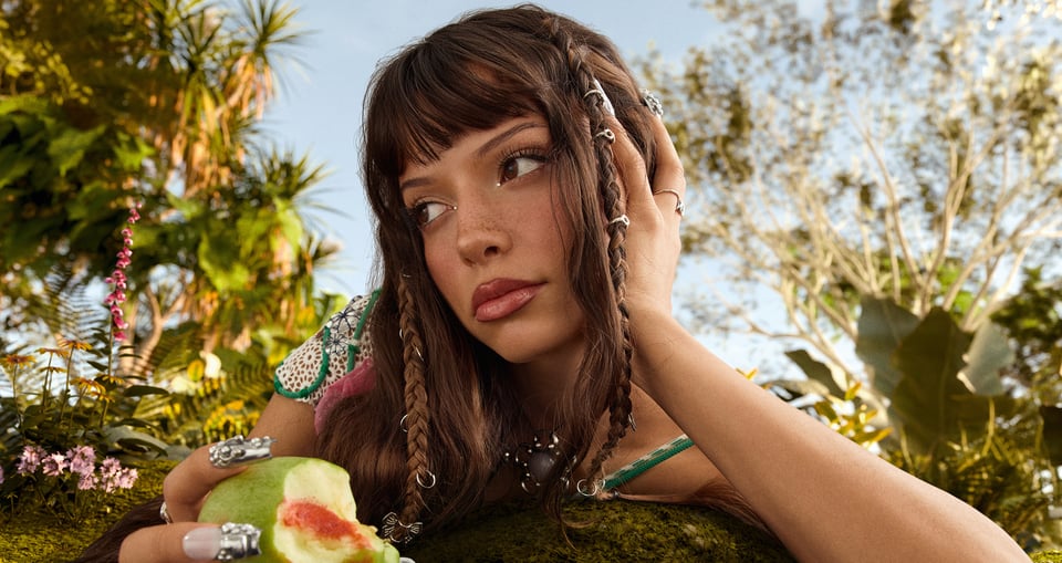Foto der Künstlerin, wie sie eine Frucht isst, im Hintergrund einige Pflanzen.