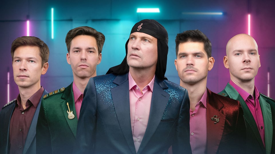 Fünf Männer in verschiedenfarbigen Anzügen vor einer Wand mit bunten Neonröhren