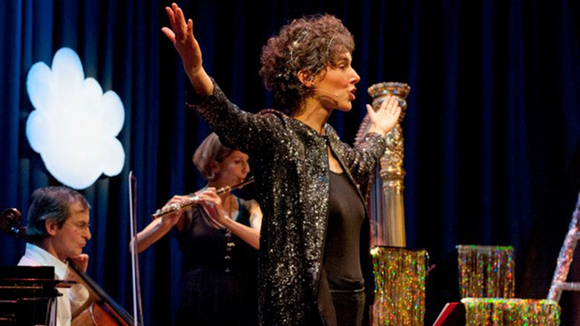 Drei Personen auf einer Bühne, im Hintergrund eine weiße Wolke