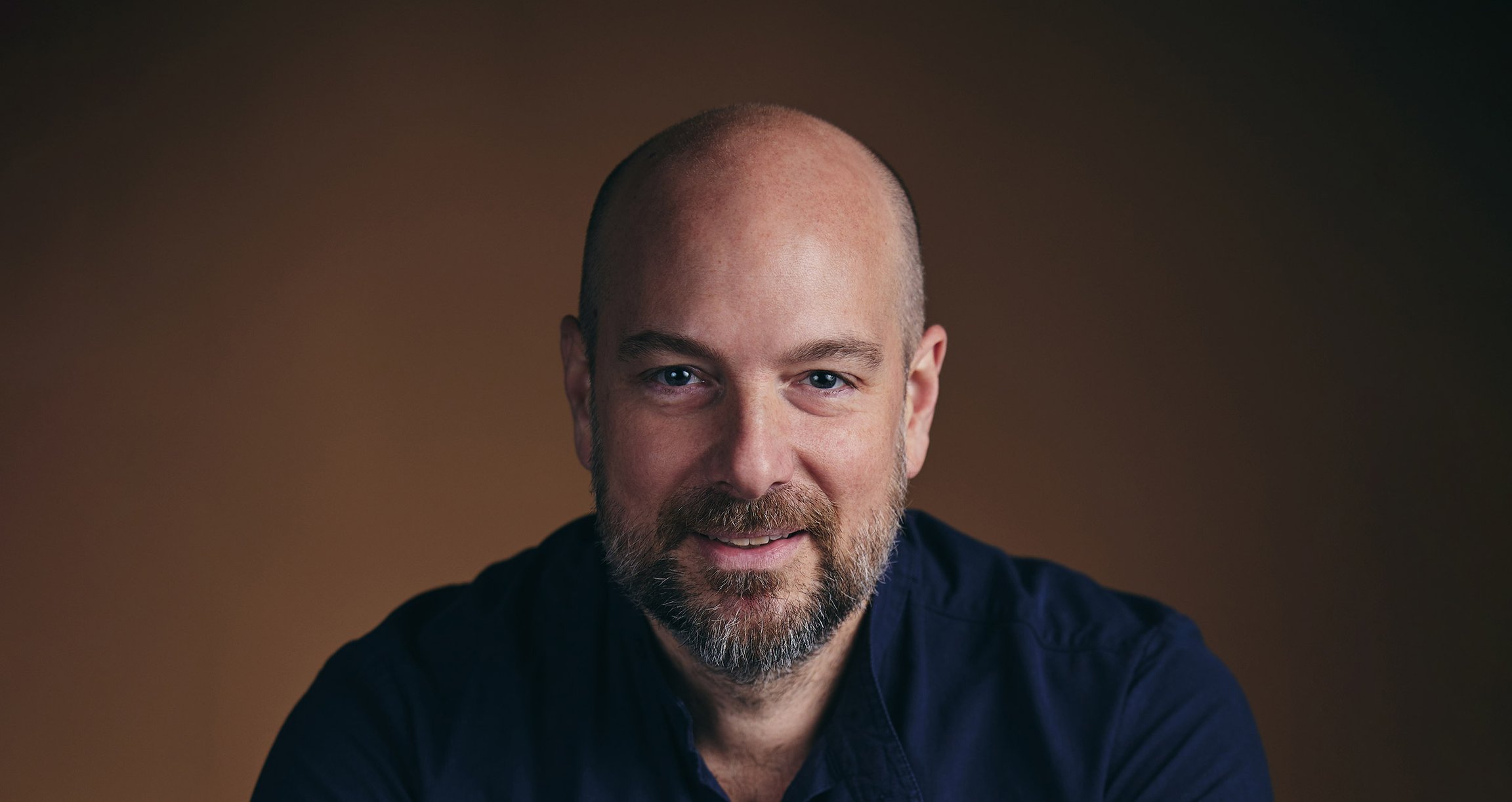 Portrait von Mann mit dunkelblauem Hemd und braunem Hintergrund