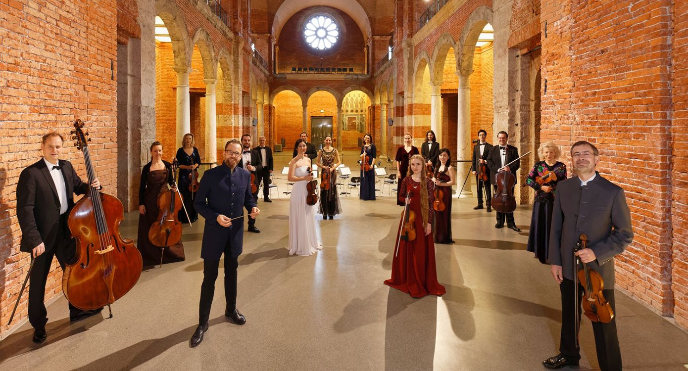 Foto einer Gruppe von Personen mit Instrumenten in einem alten Gebäude mit Säulen und Bögen