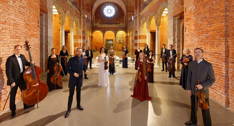 Foto einer Gruppe von Personen mit Instrumenten in einem alten Gebäude mit Säulen und Bögen