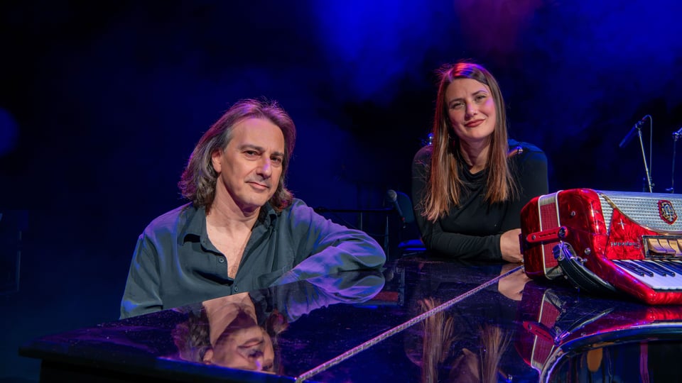 Pippo Pollina und Elisa Sandrini an einem Konzertflügel mit rotem Akkordeon auf einer blau beleuchteten Bühne.