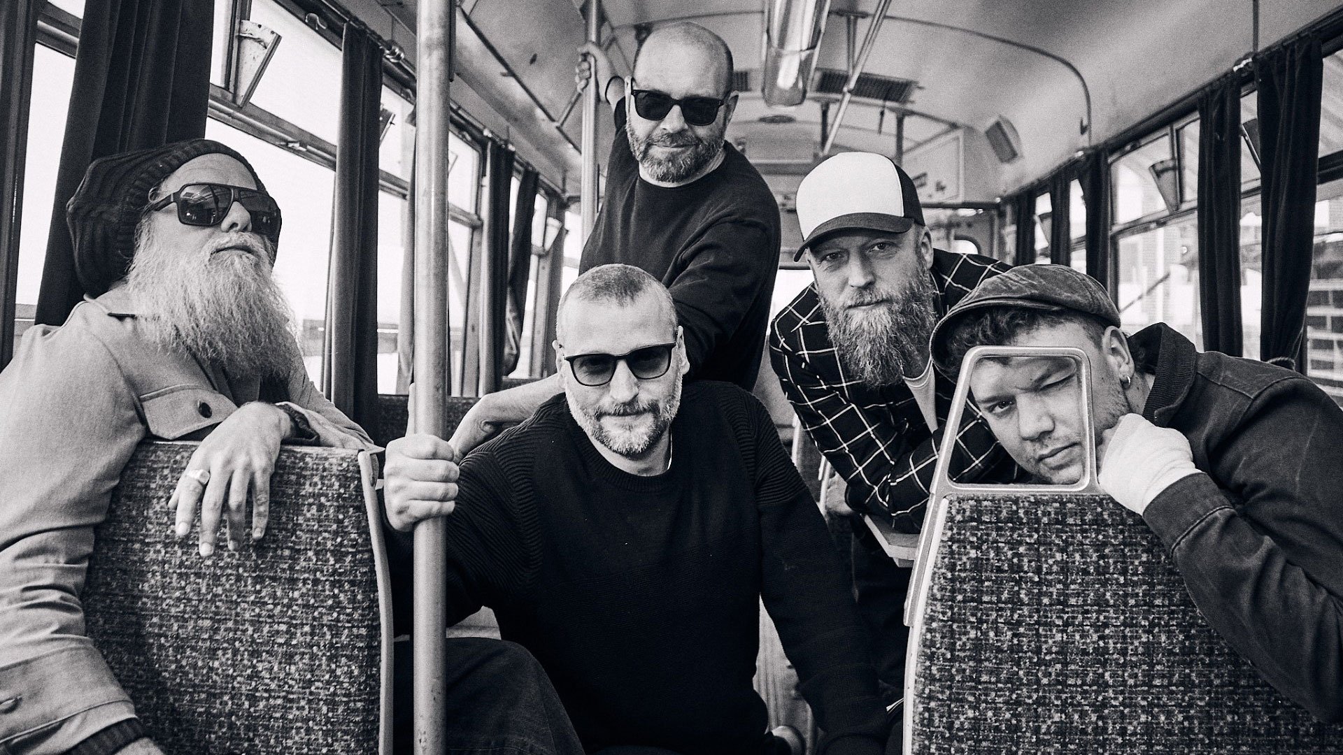 Schwarz-weiss Foto der fünf Bandmitglieder von Jaya The Cat in einer Straßenbahn zwischen Sitzreihen und Haltestangen