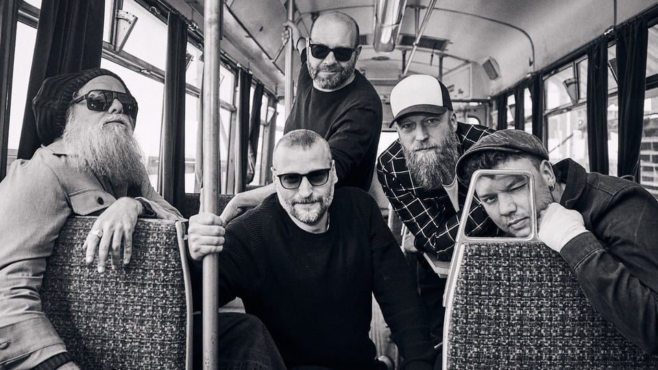 Schwarz-weiss Foto der fünf Bandmitglieder von Jaya The Cat in einer Straßenbahn zwischen Sitzreihen und Haltestangen