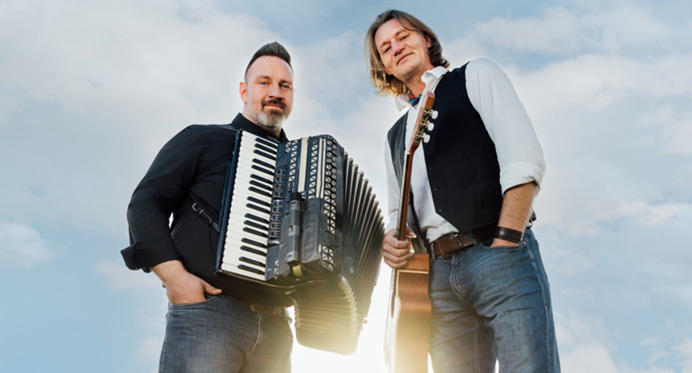 Die zwei Künstler mit Instrumenten und im Hintergrund ein blauer Himmel