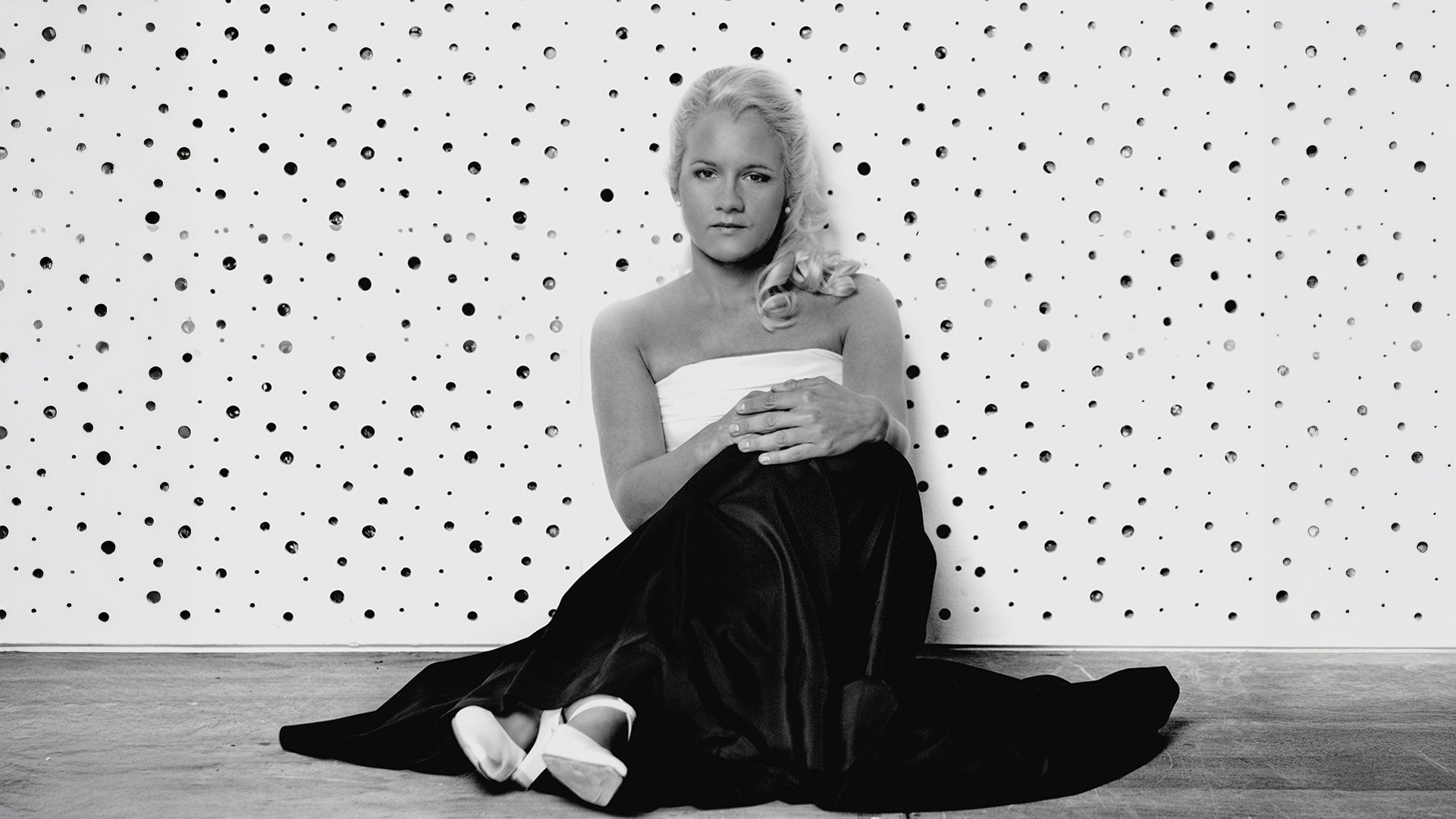 Schwarz-weiss Bild der Künstlerin vor einer Wand mit Tupfen sitzend 