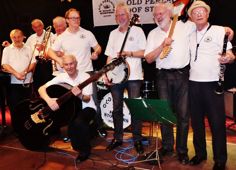 Acht Musiker in weissen Shirts und dunklen Hosen mit Instrumenten auf Bühne