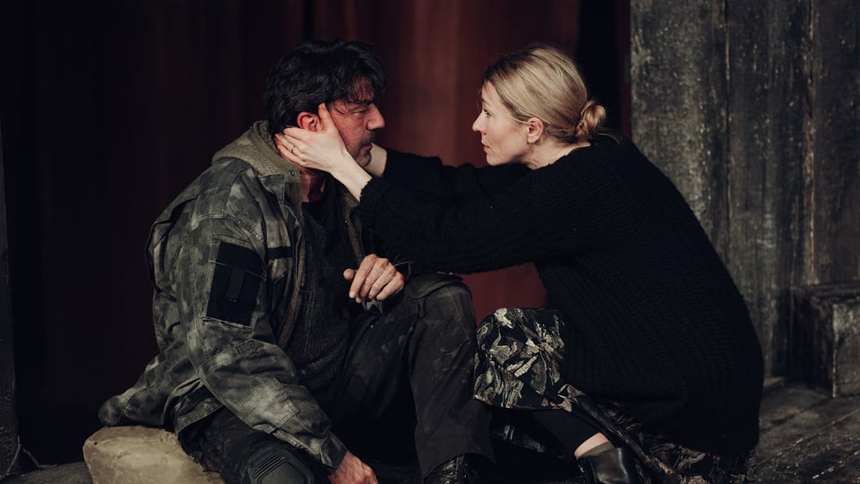 Ein Darsteller in Armeelleidung und eine Darstellerin, die seinen Kopf in die Hände nimmt