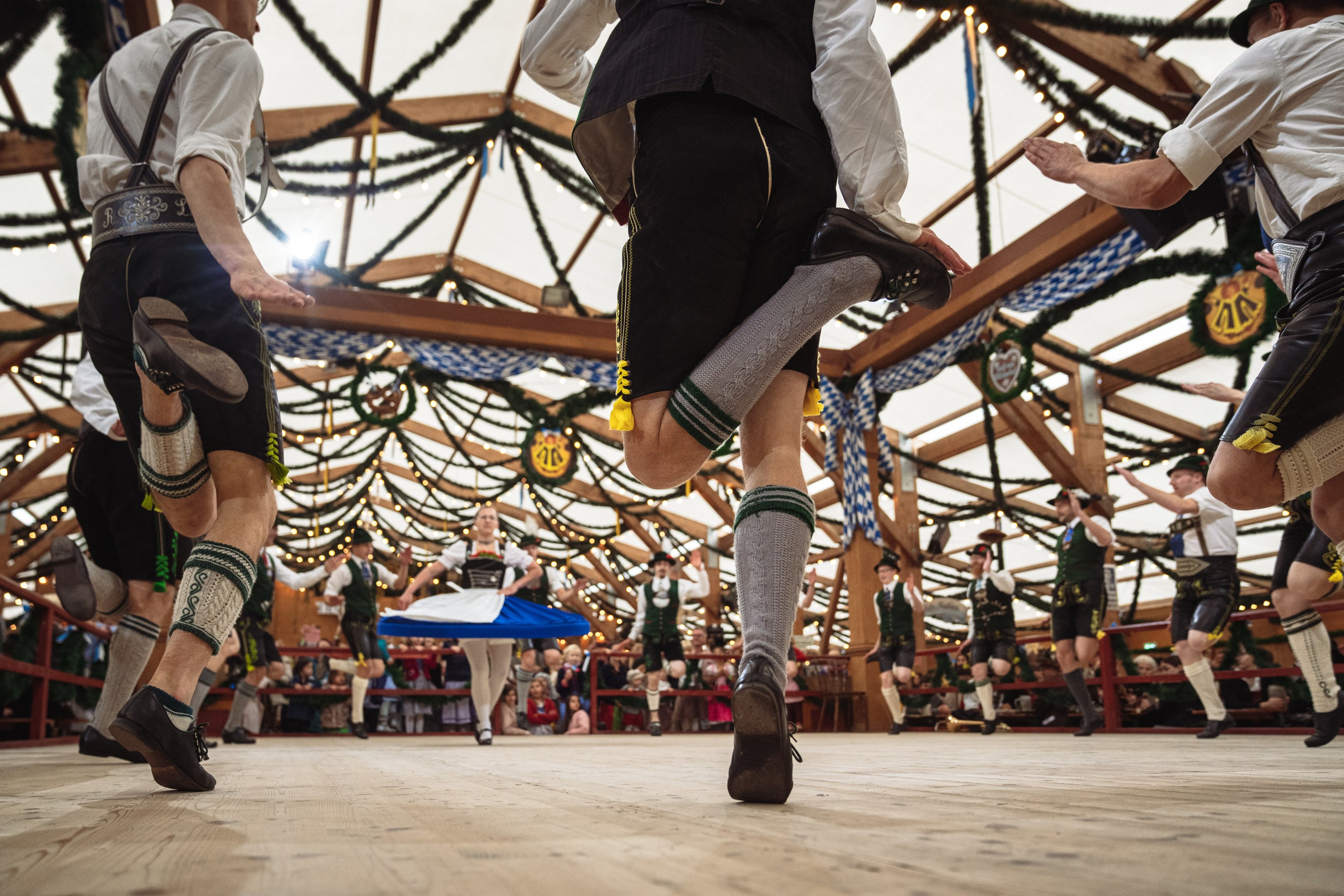 Mehrere Personen in Tracht tanzen auf einer Bühne im Zelt auf der Oiden Wiesn