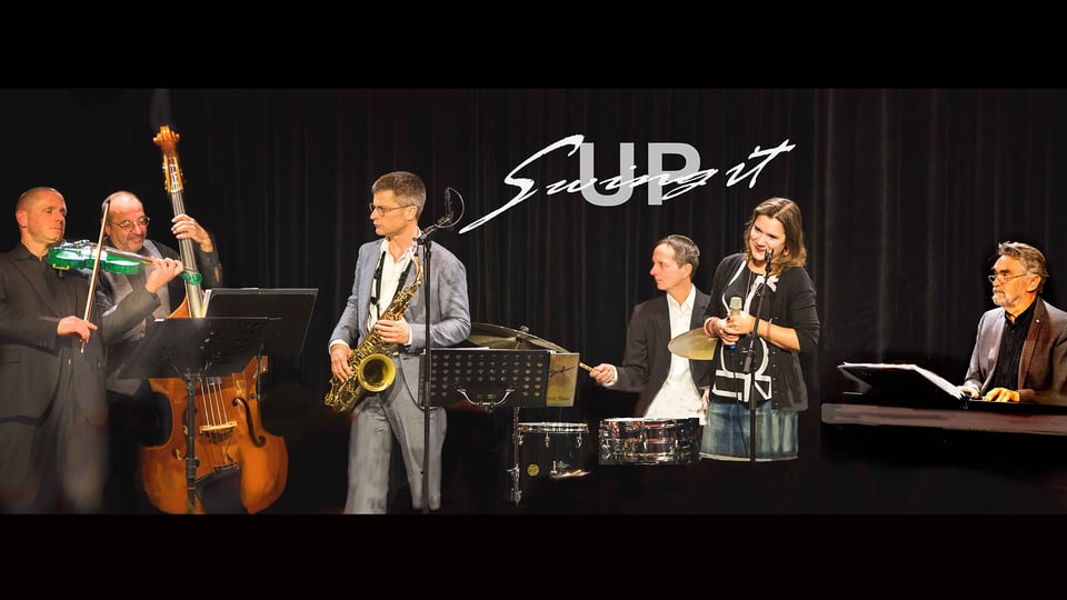 Sechs MusikerInnen mit Instrumenten auf einer Bühne mit schwarzem Vorhang und Aufschrift Swing It Up