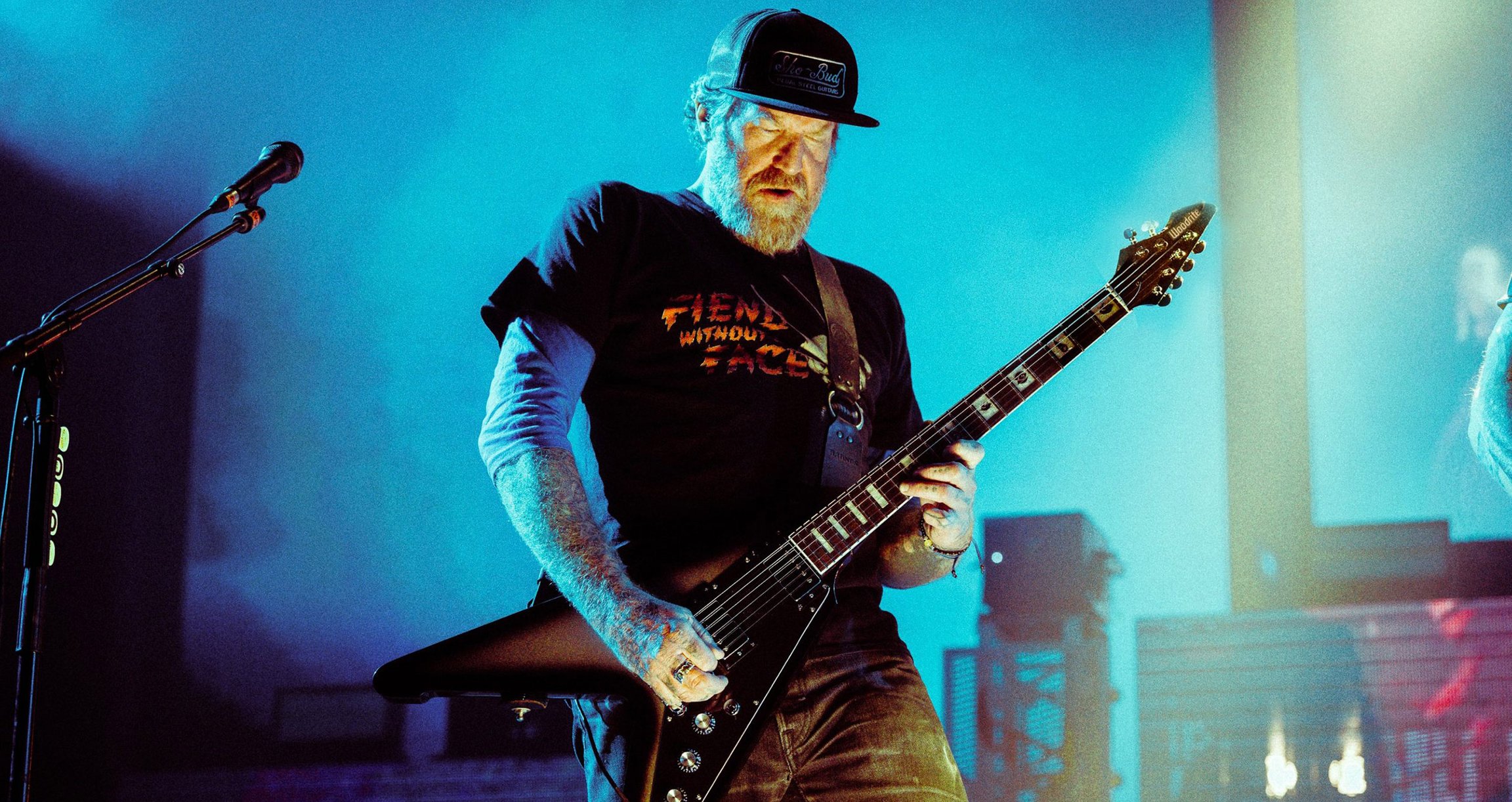 Mann mit Kappe und Gitarre auf Bühne mit blauem Licht