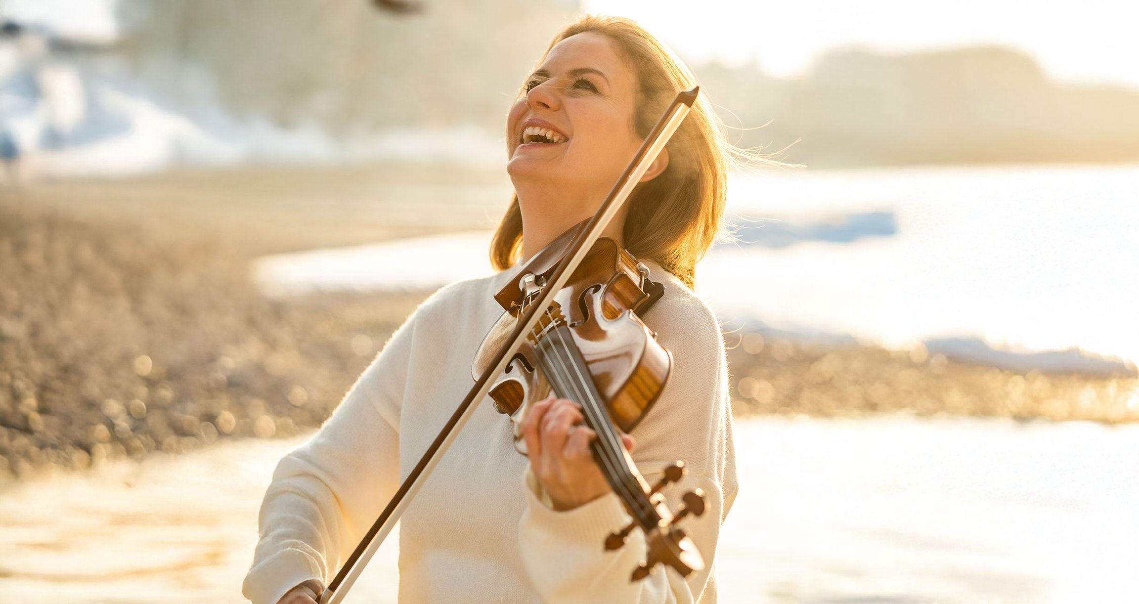 Künstlerin mit Violine, lachend am Strand