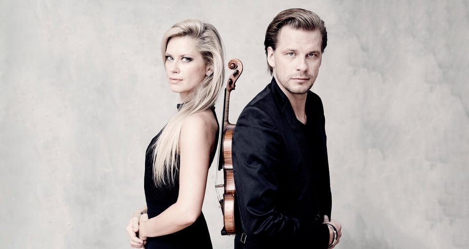 Foto der beiden Künstler mit einem Instrument in der Mitte auf beigem Hintergrund