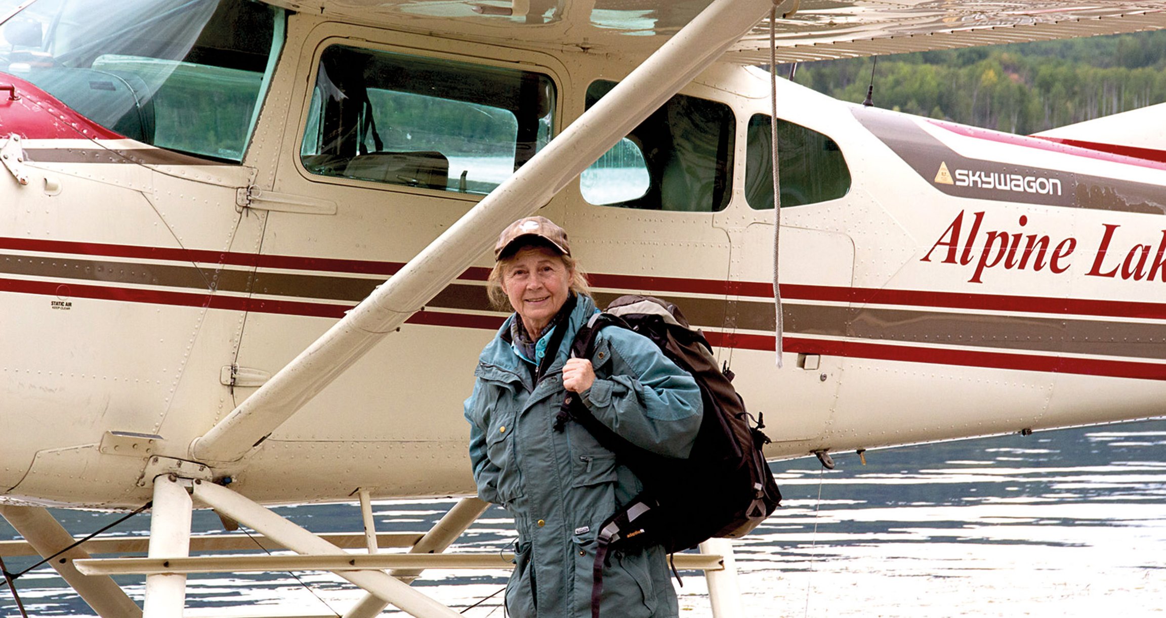 Eine Frau mit einem Wanderrucksack, im Hintergrund ein kleines Flugzeug