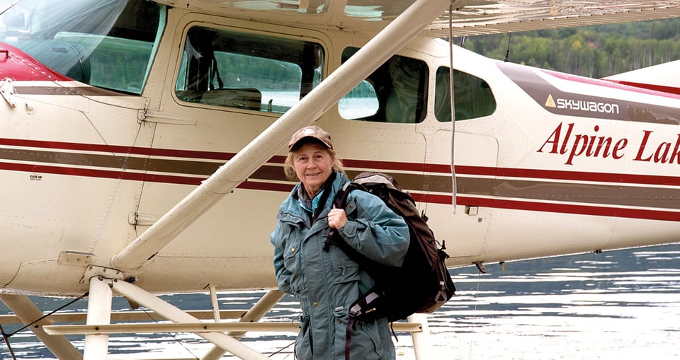 Eine Frau mit einem Wanderrucksack, im Hintergrund ein kleines Flugzeug