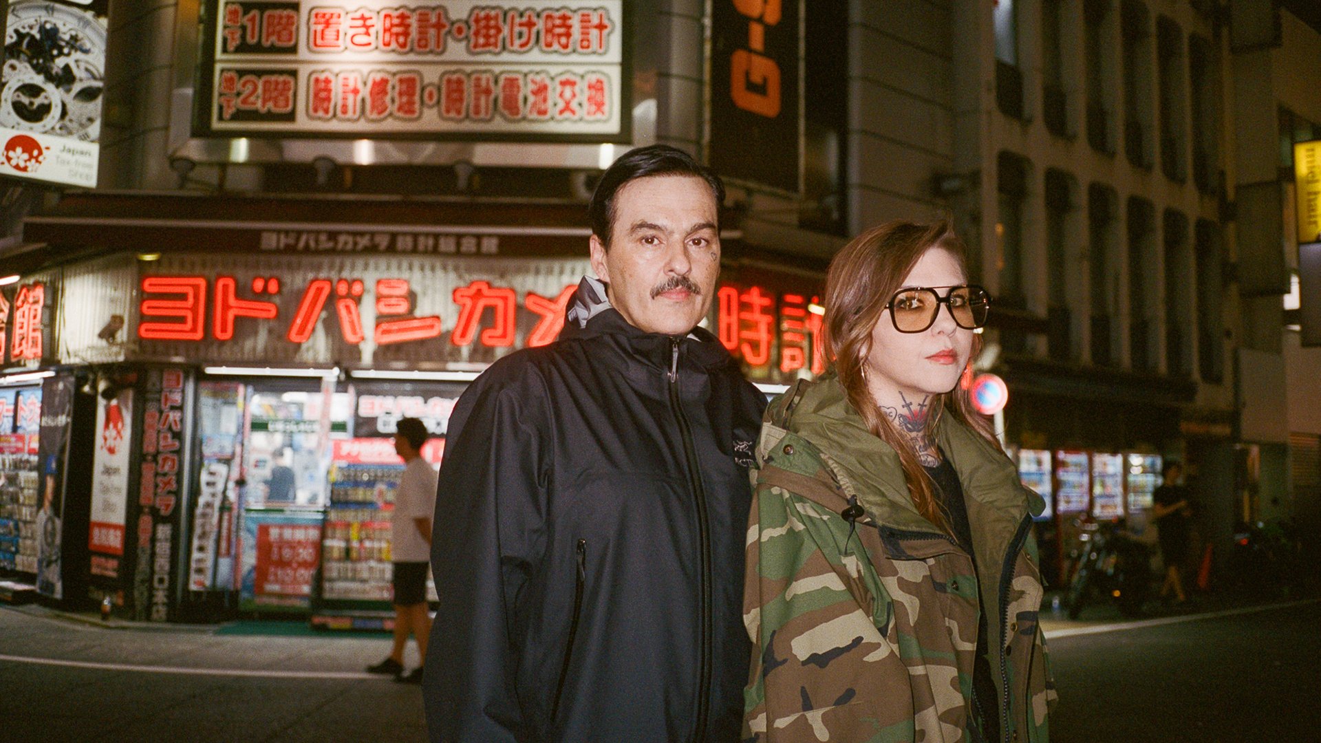 Zwei Personen auf einer Straße vor bunten Leuchtreklamen