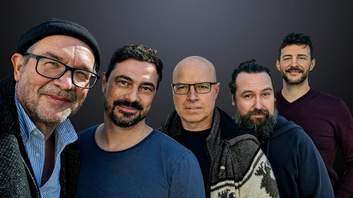 Fünf Personen stehen dicht nebeneinander vor dunklem Hintergrund und blicken in die Kamera