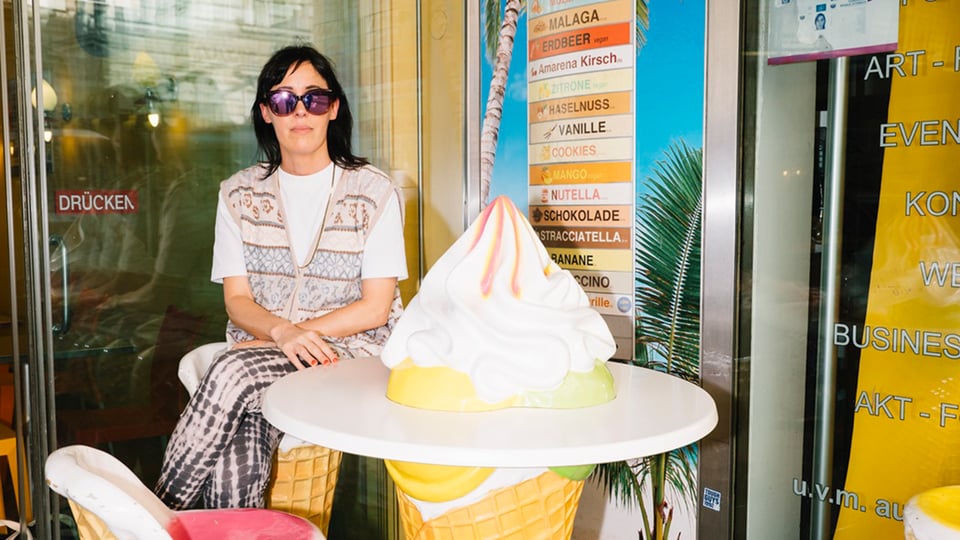 Eva Karl Faltermeier mit Sonnenbrille sitzt an einem Tisch, der eine große Eiswaffel mit Eis darstellt