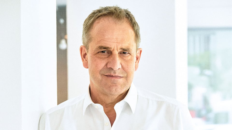 Porträt Stephan Schad in weißem Hemd, vor hellem Innenraum mit weißen Wänden und weichem Tageslicht 