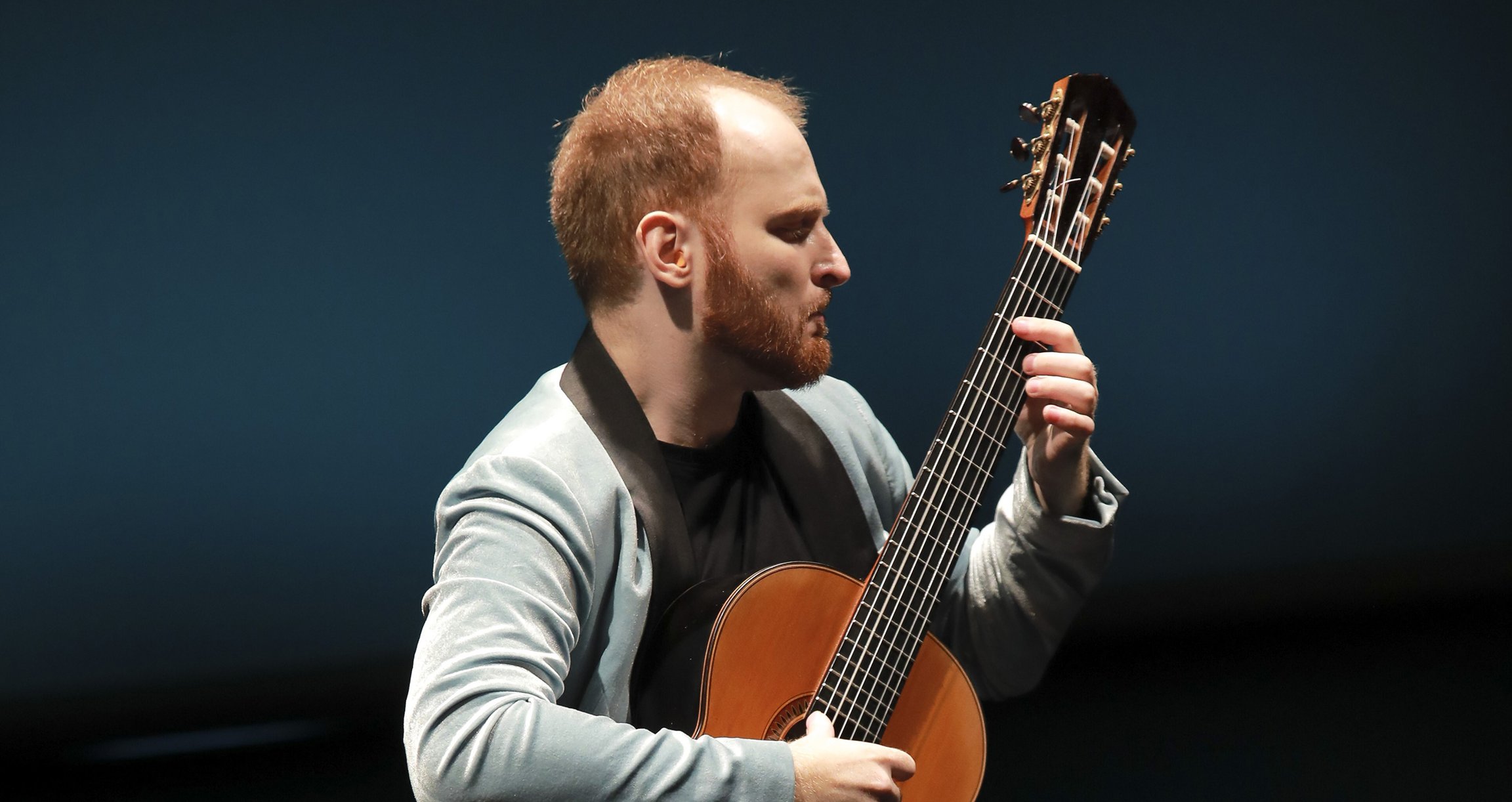 Mann mit Gitarre vor dunklem Hintergrund