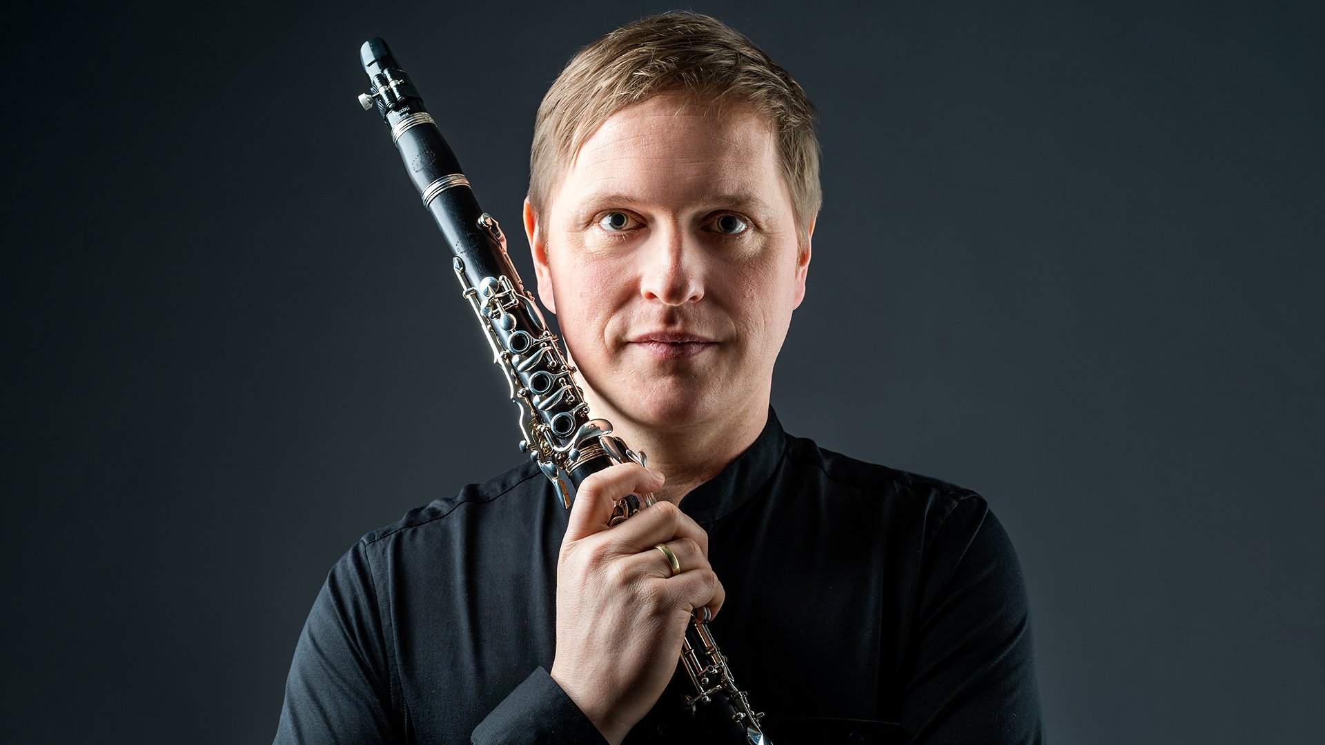 Der Künstler in dunklem Hemd mit Instrument vor dunklem Hintergrund