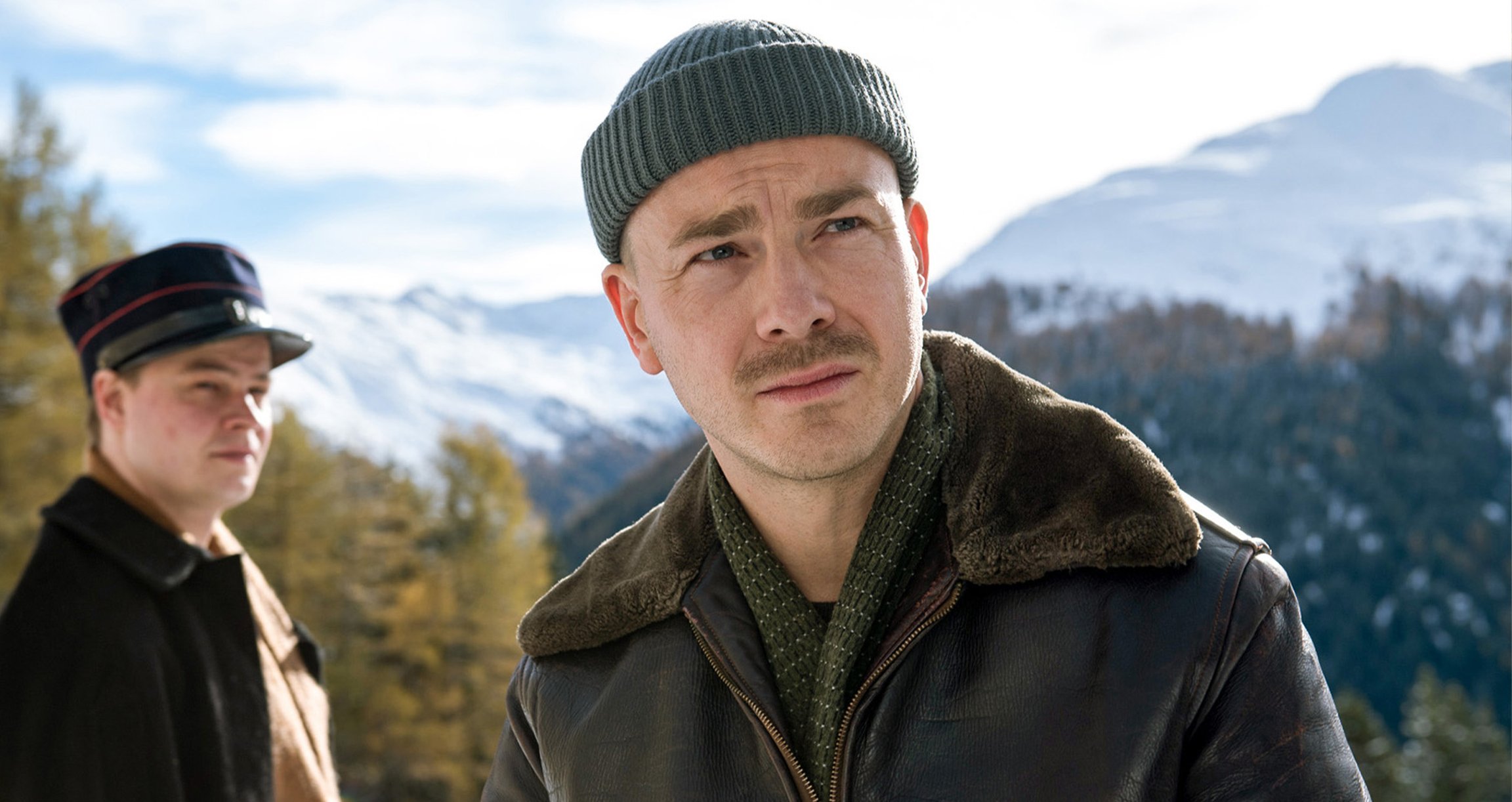 ein Bild von einem Jungen mit einer anderen Person im Hintergrund und einer Berglandschaft im Hintergrund