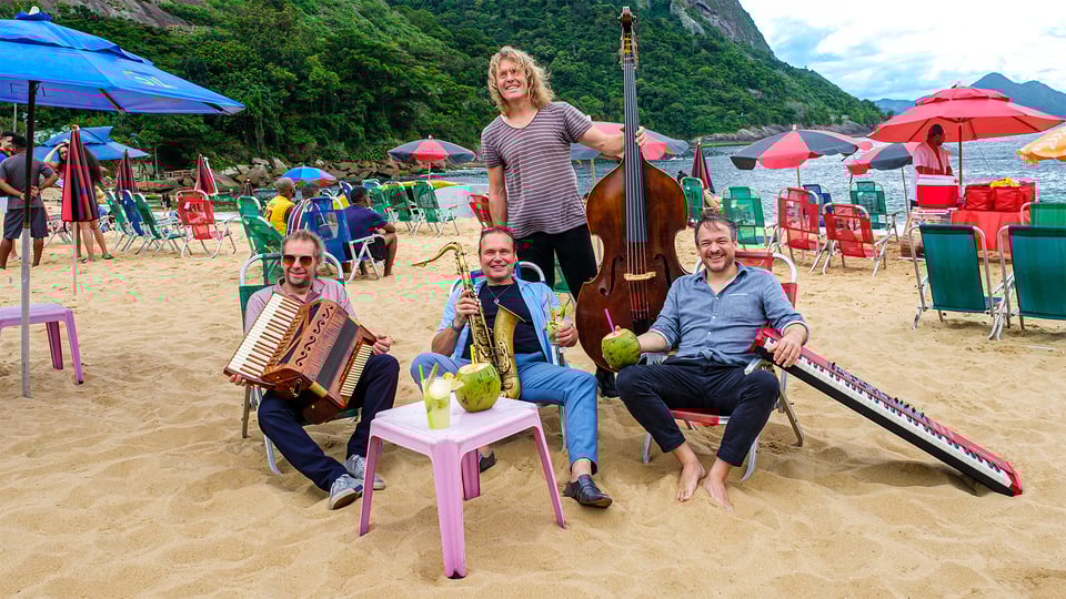 Die vier Musiker mit Instrumenten an einem Strand mit zahlreichen Sonnenschirmen