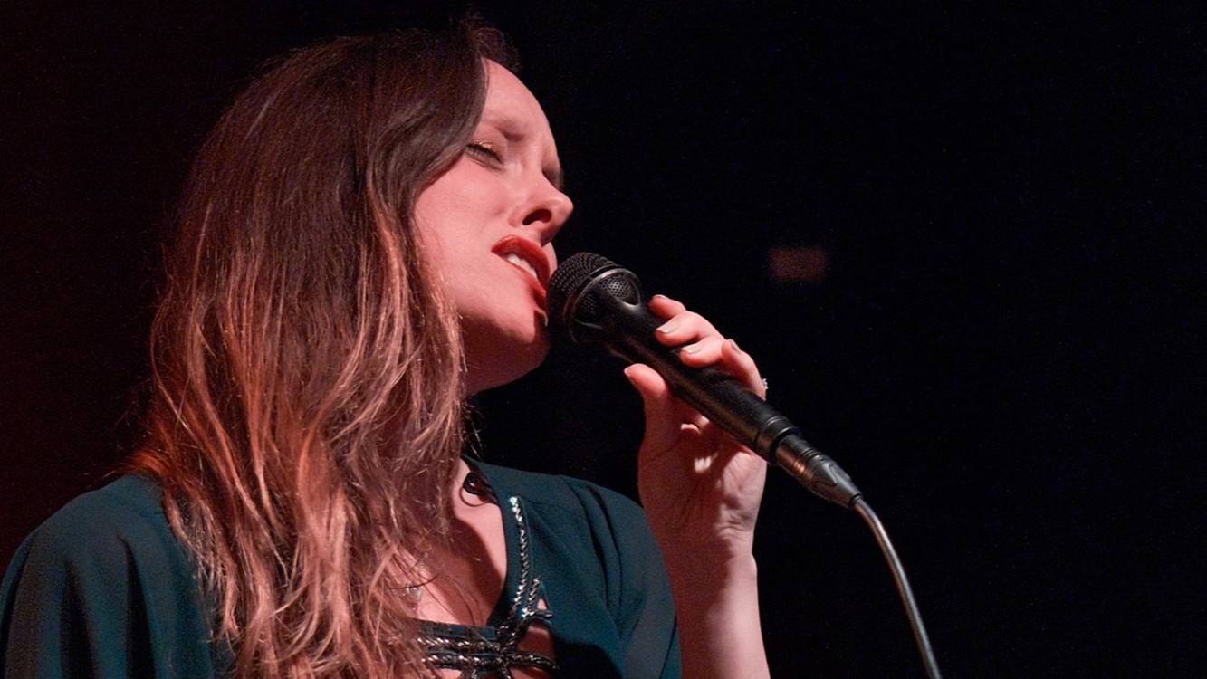 Foto für die Veranstaltung Isabel Casas mit der Künstlerin mit einem Mikrofon vor schwarzem Hintergrund