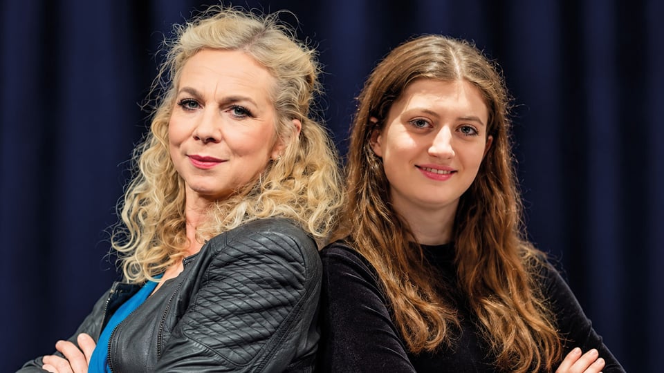 Franziska Ball und Bianca Seufert in dunkler Kleidung stehen aneinandergelehnt und blicken in die Kamera, vor dunkelblauem Hintergrund