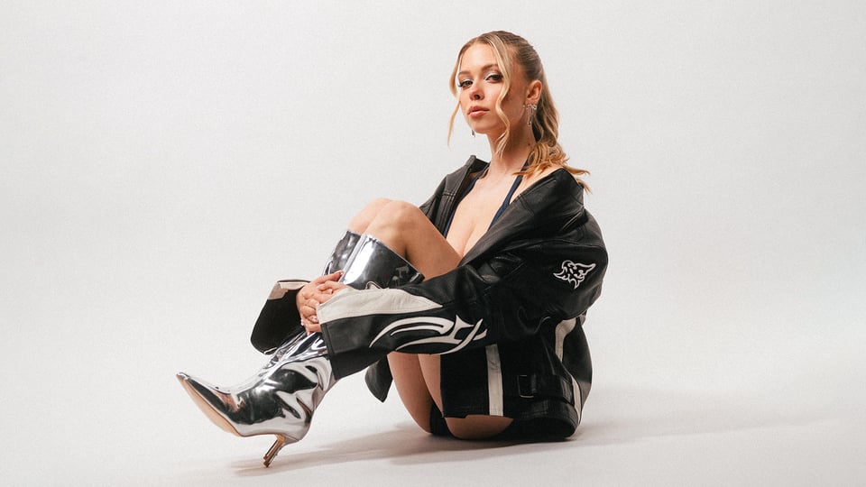 Foto für die Veranstaltung ‚KATI K‘ – sitzend auf dem Boden mit High Heels vor weißem Hintergrund